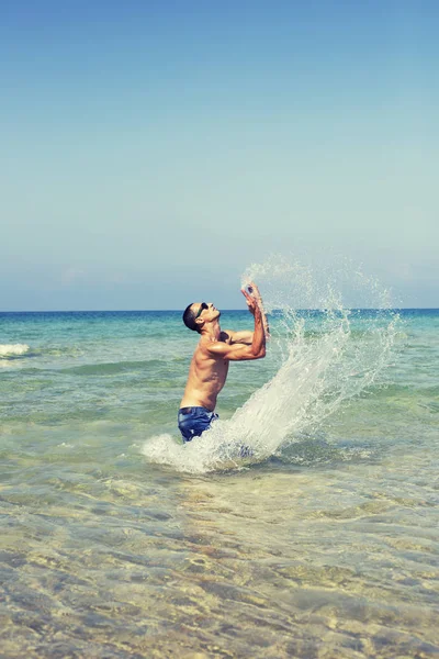 Jong macho man model atleet met gespierd sexy lichaam spelen met de golven in de zee — Stockfoto