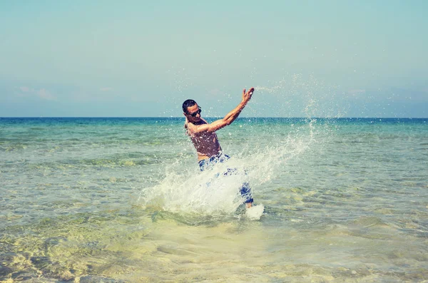 Joven macho hombre modelo atleta con muscular sexy cuerpo jugando con las olas en el mar —  Fotos de Stock