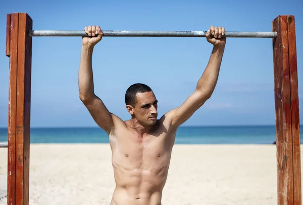 Un atleta masculino con un torso desnudo está entrenando en una barra horizontal — Foto de Stock
