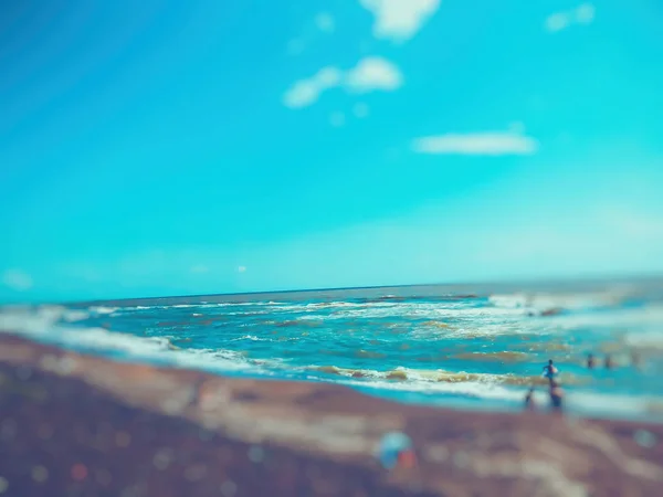 Pohled na moře při západu slunce. Lidé plavou v moři. Třpytivé vlny na písečné pláži. Letní slunečný den, efekt rozmazání — Stock fotografie