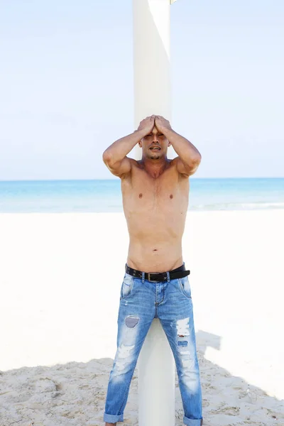 Junger muskulöser Mann in Jeanshose, der am Strand liegt und posiert — Stockfoto