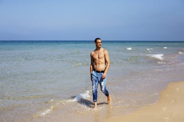Genç kaslı adam sahilde dinleniyor ve poz veriyor. Havaya zıpla