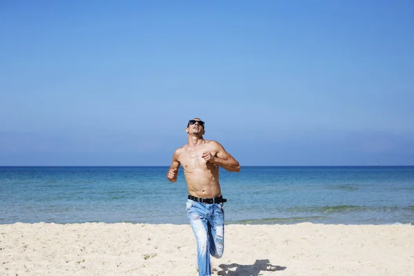 Junger muskulöser Mann, der sich ausruht und am Strand posiert. Lauf auf uns zu — Stockfoto