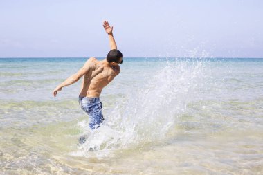 Genç kaslı adam denizde poz veriyor ve su sıçratıyor.