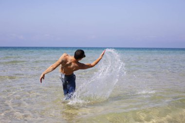 Genç kaslı adam denizde poz veriyor ve su sıçratıyor.