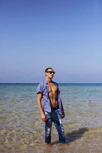 Joven musculoso descansando y posando en la playa. Un joven camina junto al mar — Foto de Stock