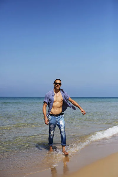 Jonge gespierde man rustend en poserend op het strand. Een jongeman loopt langs de zee. — Stockfoto