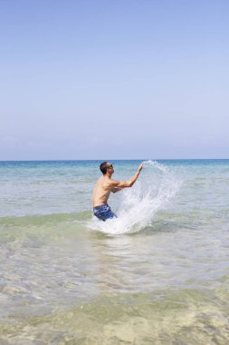 Genç kaslı adam denizde poz veriyor ve su sıçratıyor.