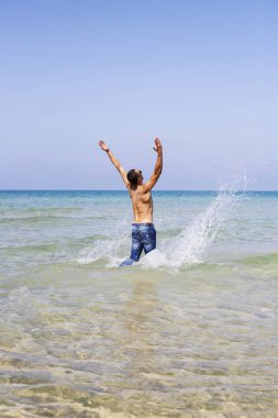 Genç kaslı adam denizde poz veriyor ve su sıçratıyor.