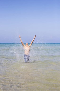 Genç kaslı adam denizde poz veriyor ve su sıçratıyor.