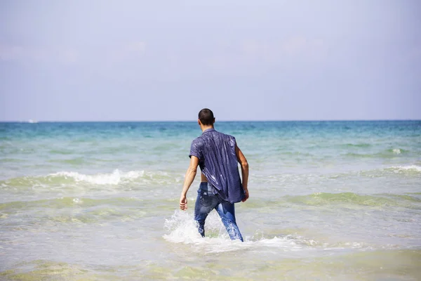 Giovane uomo muscoloso che riposa e posa sulla spiaggia. Un giovane uomo cammina in riva al mare — Foto Stock