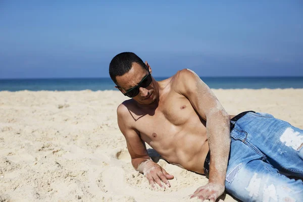 Junger muskulöser Mann ruht sich aus und posiert am Strand — Stockfoto