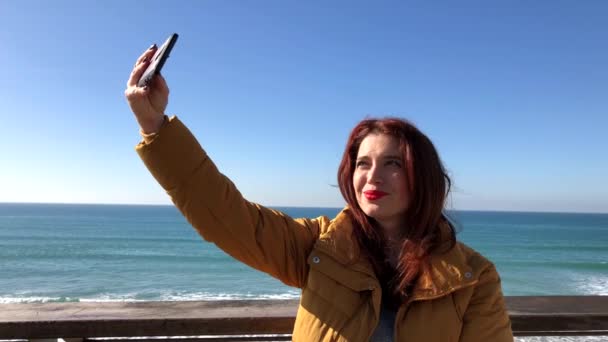 红头发的漂亮女人在大海的背景下自拍 — 图库视频影像
