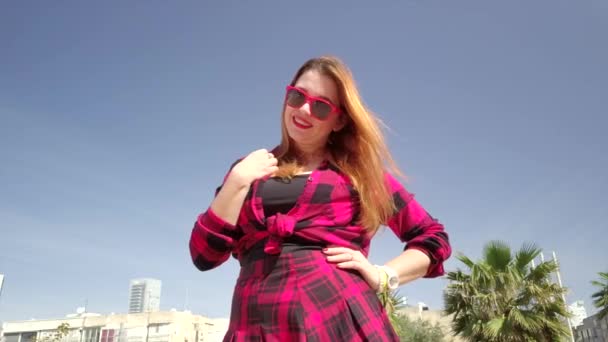 Junge Frau mit Sonnenbrille steht gegen den Himmel — Stockvideo