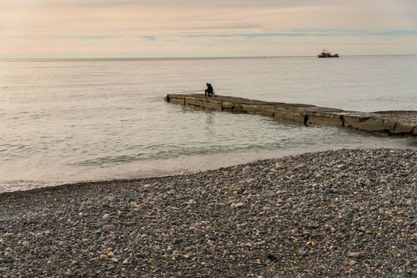 Dalgakıran şehir Sohum, Abhazya'da, Beach kıyısında oturan balık yalnız bir balıkçı yakalar.