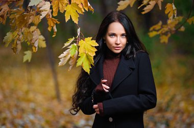 Bordo örgü süveterli bir esmer sonbahar ormanında yürüyor. Sonbaharda terk edilmiş bir binada Esmer