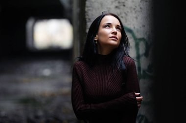 Bordo örgü süveterli bir esmer sonbahar ormanında yürüyor. Sonbaharda terk edilmiş bir binada Esmer