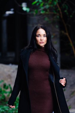 Bordo örgü süveterli bir esmer sonbahar ormanında yürüyor. Sonbaharda terk edilmiş bir binada Esmer