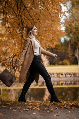 Sonbahar bej ceketli bir sarışın parkta yürüyor. Mevsimlik fotoğraf. Cazibe Moda