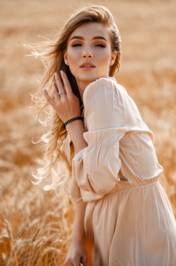 Buğday tarlasında büyük bir hasır şapkayla bej bir Midi elbiseyle çekici ve güzel bir kız.