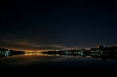 Gece şehrinde göl yıldızlı gökyüzünün altında.