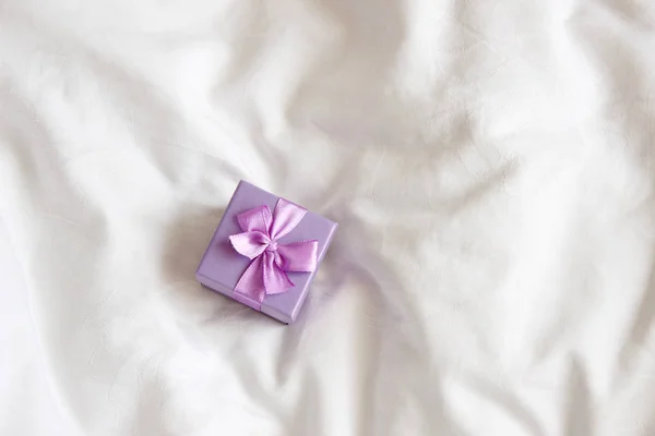 Jewelry Gift box close up. Present box for holidays, decorated with white ribbon bow. Valentine\'s Day gift, International Women\'s Day gift over white bed linen background.