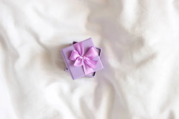 Jewelry Gift box. Present box for holidays, decorated with purple ribbon bow. Valentine\'s Day gift, International Women\'s Day gift over white bed linen background. Valentine\'s Gift closeup