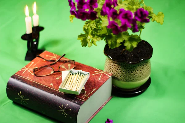 still life with flower book candles and glasses on a green background