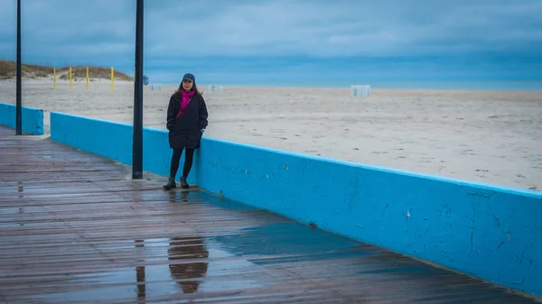 Woman on boardwalk with sea, beach and volley ball courts behind her