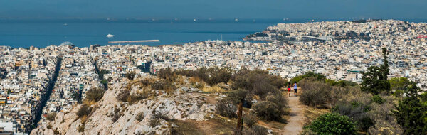 Женщина и подросток бегут в Афинах через парк с Эгейским морем и городом на заднем плане
