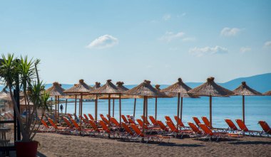 Turuncu plaj sandalyeleri ve arka planda dağlar ile denizde doğal şemsiye