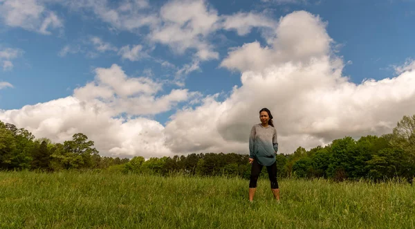 Mujer de pie en el campo verde con nubes detrás — Foto de Stock