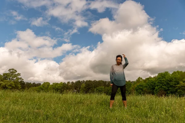 Mujer de pie en el campo verde con nubes detrás — Foto de Stock