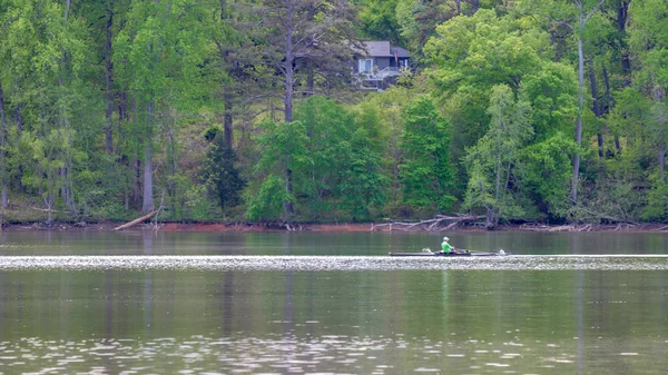 Man in crew boat on lake rowing with trees in the background