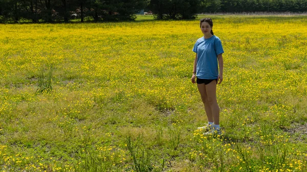 Adolescente de pie en campo grande con flores amarillas y árboles en th — Foto de Stock