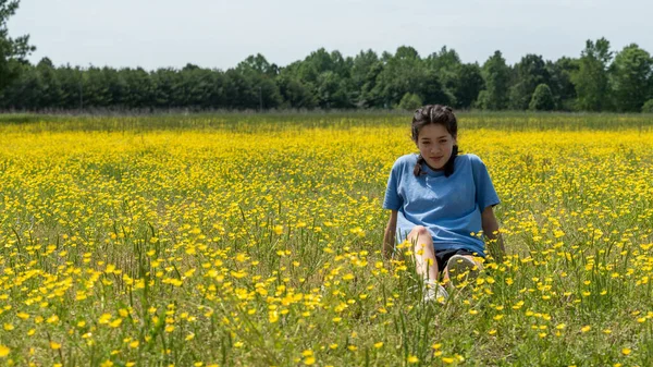 Chica adolescente sentada en un campo grande con flores amarillas y árboles i — Foto de Stock
