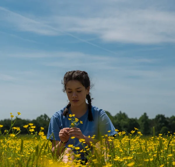 Chica adolescente sentada en un campo grande con flores amarillas y árboles i — Foto de Stock