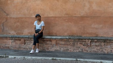 Şapkalı bir kadın güzel bir teracota duvarının önünde oturuyor ve Bolonya 'daki fotoğrafçıya bakıyor.