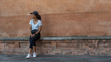 Şapkalı bir kadın güzel bir teracota duvarının önünde oturuyor Bologna İtalya 'da fotoğrafçıdan gözünü kaçırıyor.
