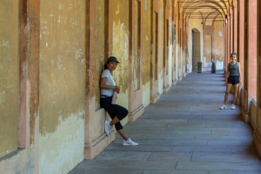 Şapkalı anne elinde termosla duvara yaslanırken genç kız Bologna İtalya 'da ona bakıyor.