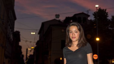 Siyah bluzlu genç Asyalı taş caddede duruyor. Bologna İtalya 'da gece vakti siyah bluzla binanın önünde.