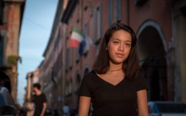 Siyah bluzlu genç Asyalı Bologna İtalya 'da taş caddenin önünde siyah bluzla dikiliyor.