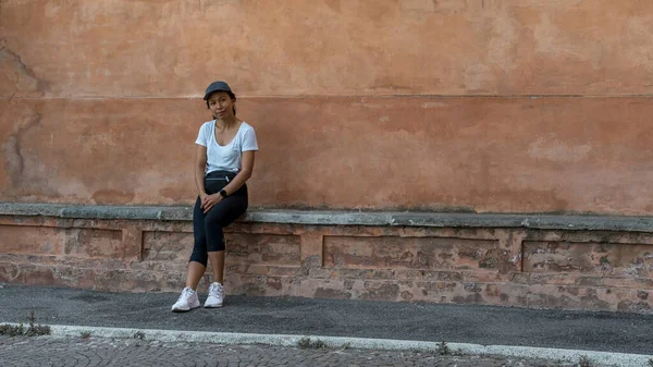 Şapkalı bir kadın güzel bir teracota duvarının önünde oturuyor ve Bolonya 'daki fotoğrafçıya bakıyor.