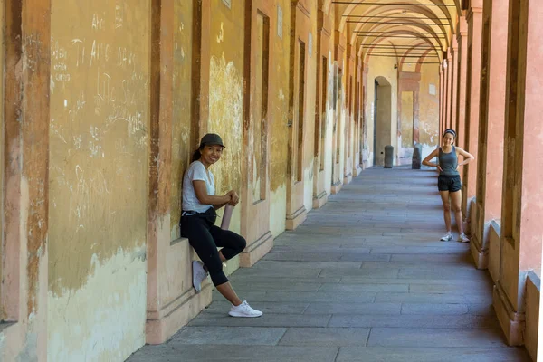 Şapkalı anne elinde termosla duvara yaslanırken genç kız Bolonya İtalya 'da kalçasında elleriyle ona bakıyor.
