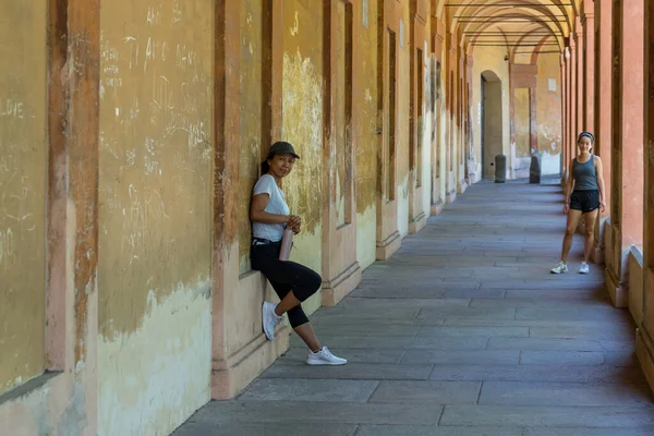 Şapkalı anne elinde termosla duvara yaslanırken genç kız Bologna İtalya 'da ona bakıyor.