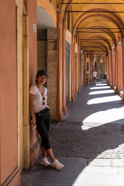 Tişörtlü, spor ayakkabılı, siyah şapkalı, güneş gözlüklü bir kadın Bologna İtalya 'daki The Portacoes Promanade' ın yanında duruyor.