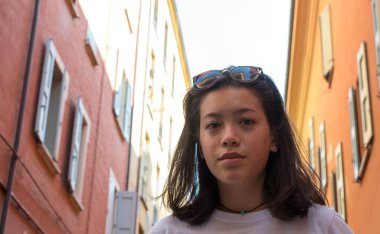 Kafasında güneş gözlüğü olan Asyalı Amerikalı bir gencin portresi eski binaların önünde gülümsüyor.