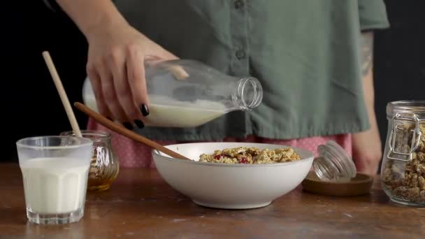Самка вручную наливает молоко в миску с гранолой — стоковое видео