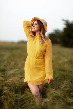 Buğday tarlasında parlak sarı elbisesi ve hasır şapkası olan sarışın hayalperest kız..