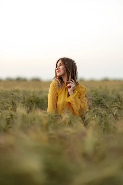 Blonde fille rêveuse dans un champ de blé portant une robe jaune vif et un chapeau de paille. — Photo